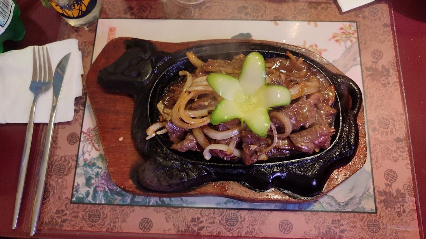 Bœuf aux oignons servi sur une plaque en fonte, garni d’une fleur de concombre